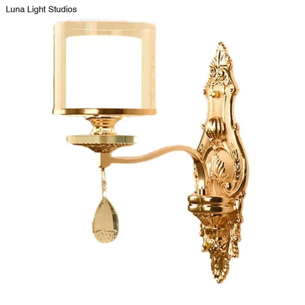 Gold-finished ornate wall mount lamp with cylindrical frosted glass shade and teardrop crystal pendant for living room