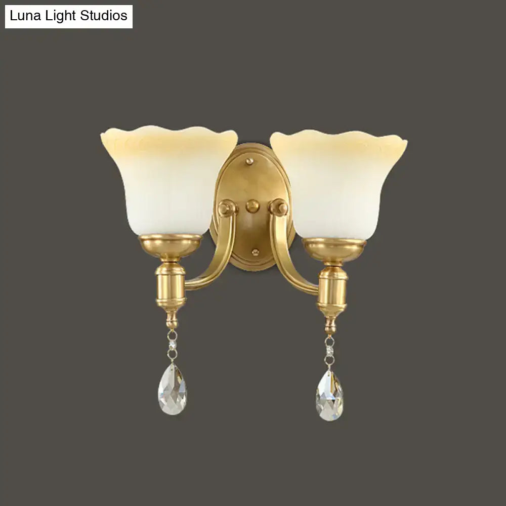 Gold-finished double-light wall lamp with blossom opaque glass shades and dangling crystal teardrop pendants for bedroom