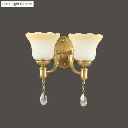 Gold-finished double-light wall lamp with blossom opaque glass shades and dangling crystal teardrop pendants for bedroom