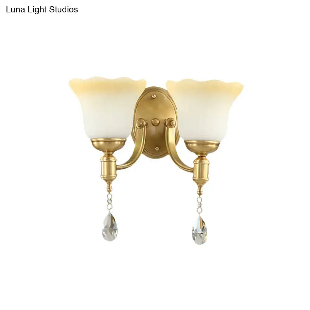 Gold-finished wall lamp with two frosted cream blossom opaque glass shades and crystal teardrop pendants for bedroom use