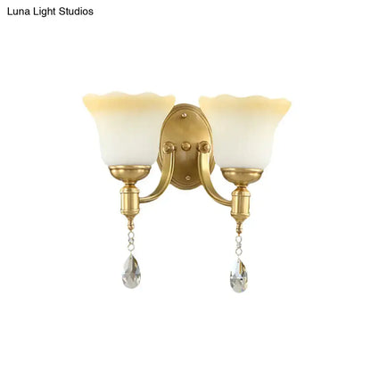Gold-finished wall lamp with two frosted cream blossom opaque glass shades and crystal teardrop pendants for bedroom use