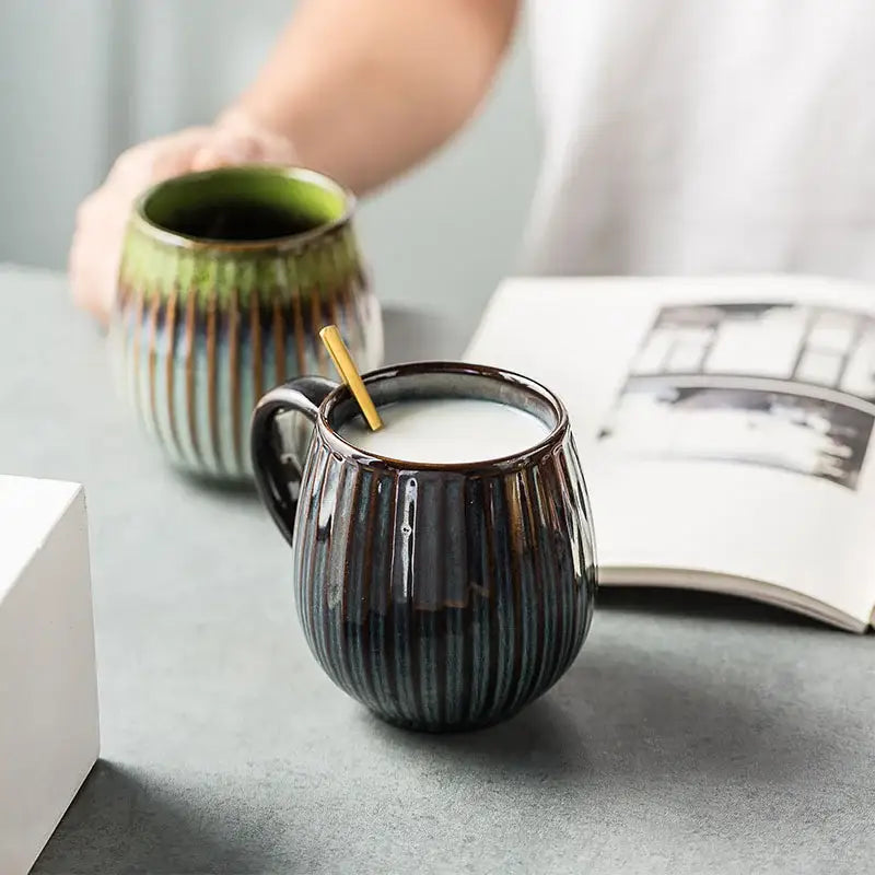 Dark ceramic coffee mug with vertical ridges and glossy gradient glaze filled with milk and wooden stirrer