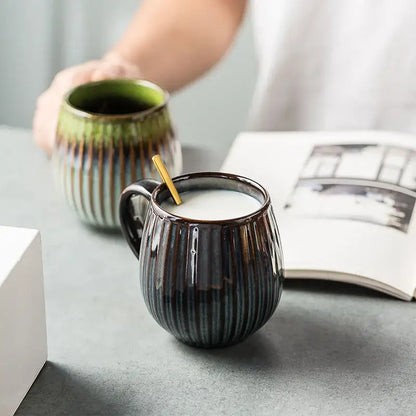 Dark ceramic coffee mug with vertical ridges and glossy gradient glaze filled with milk and wooden stirrer
