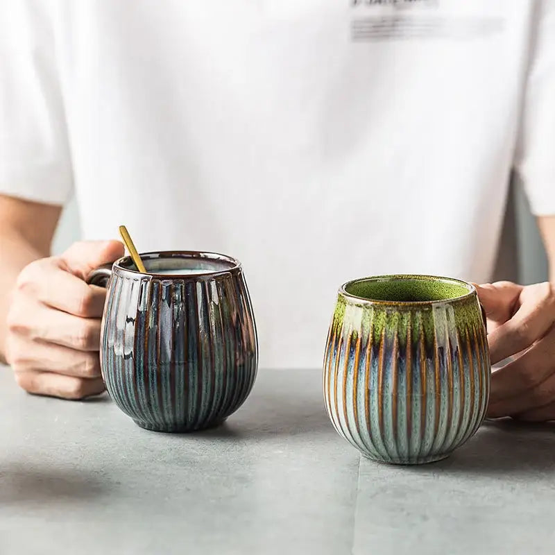 Two handcrafted ceramic coffee mugs with vertical ribbed texture and gradient glaze in blue-gray and green tones
