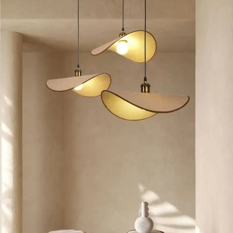 Three cream-colored decorbites hat pendant lights with brass accents and warm glow for dining room decor