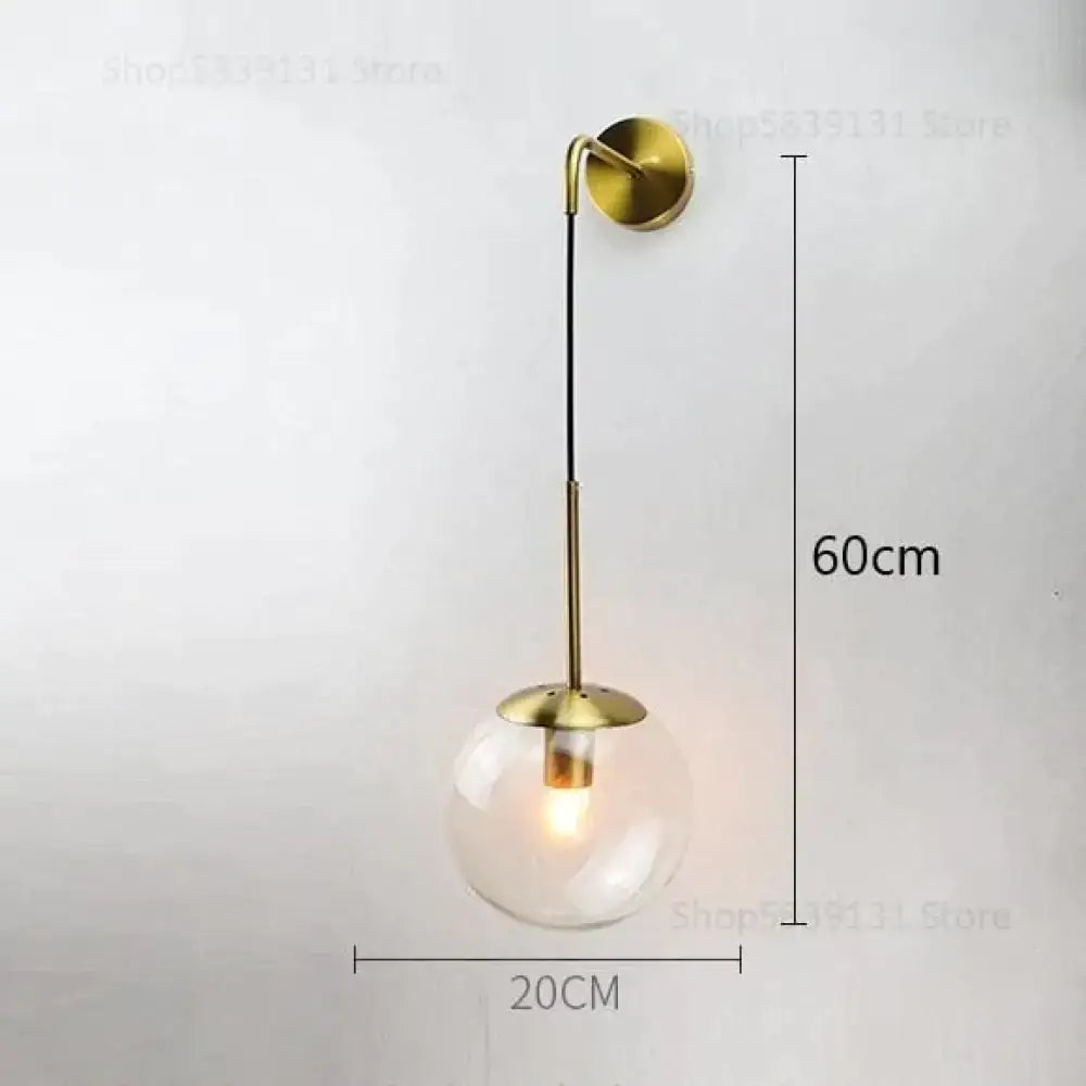 A modern brass-finished wall lamp with clear glass globe and curved arm for nordic retro modern bedroom lighting