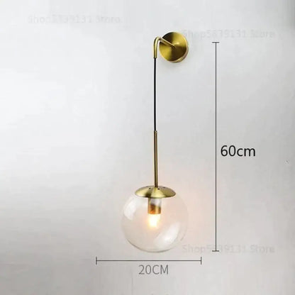 A modern brass-finished wall lamp with clear glass globe and curved arm for nordic retro modern bedroom lighting
