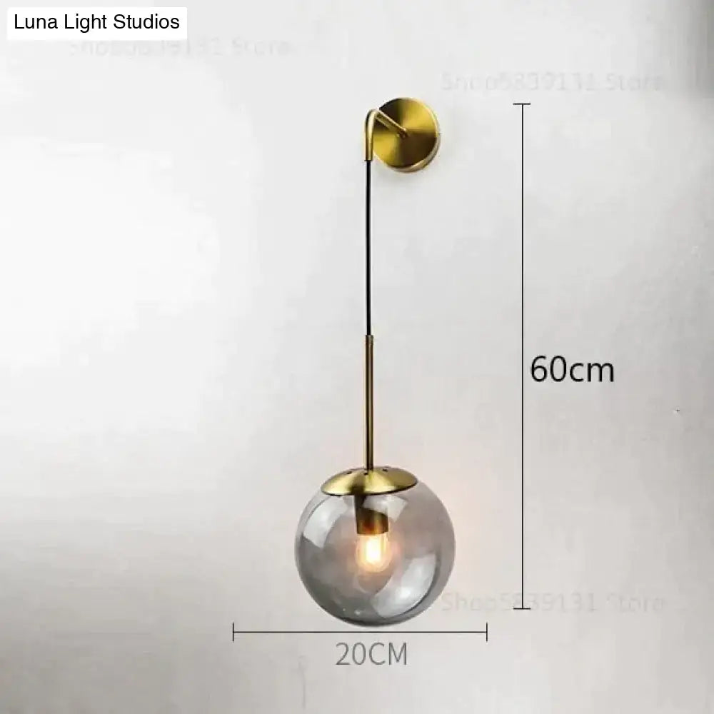 A nordic retro modern brass-finished wall lamp with a spherical smoked glass globe and adjustable arm for bedroom lighting