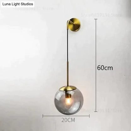 A nordic retro modern brass-finished wall lamp with a spherical smoked glass globe and adjustable arm for bedroom lighting