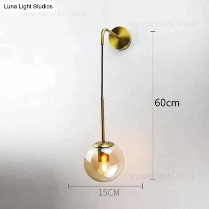 A modern brass wall lamp with a slender curved arm and smoked amber glass globe for Nordic retro modern bedroom lighting