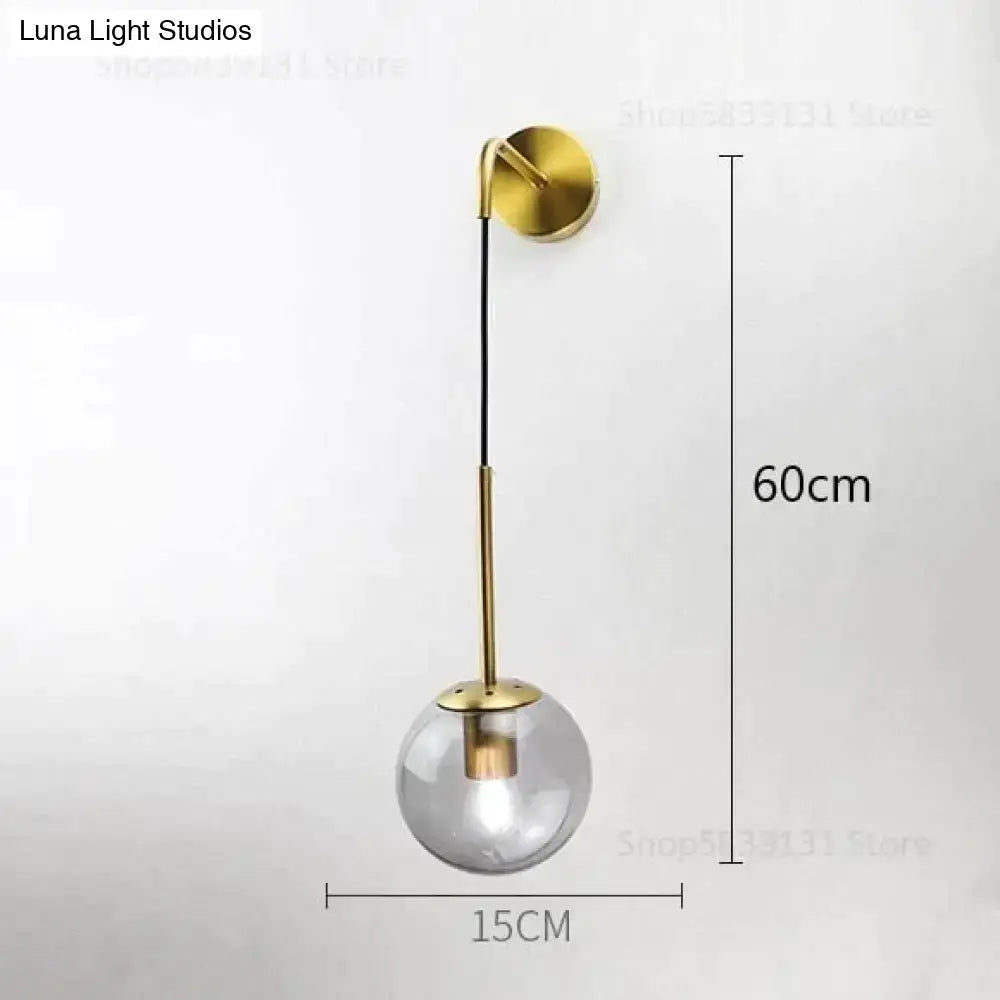 A modern brass-finished wall lamp with a smoked glass globe and slender stem for nordic retro modern bedroom lighting