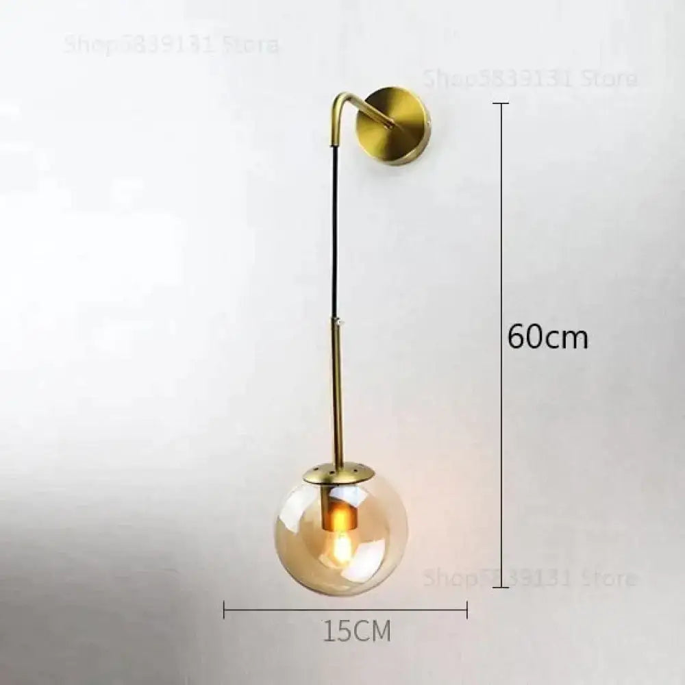 A modern brass wall lamp with a spherical amber glass globe and exposed filament bulb for bedroom lighting