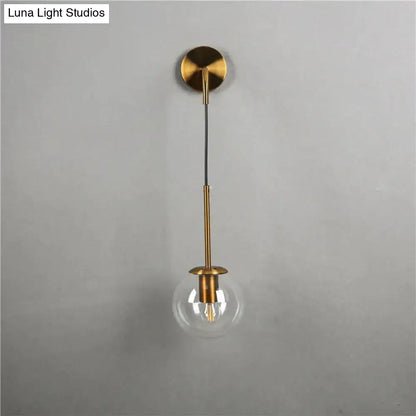 Gold-toned retro modern glass wall lamp with clear globe and brass stem for nordic retro modern bedroom lighting