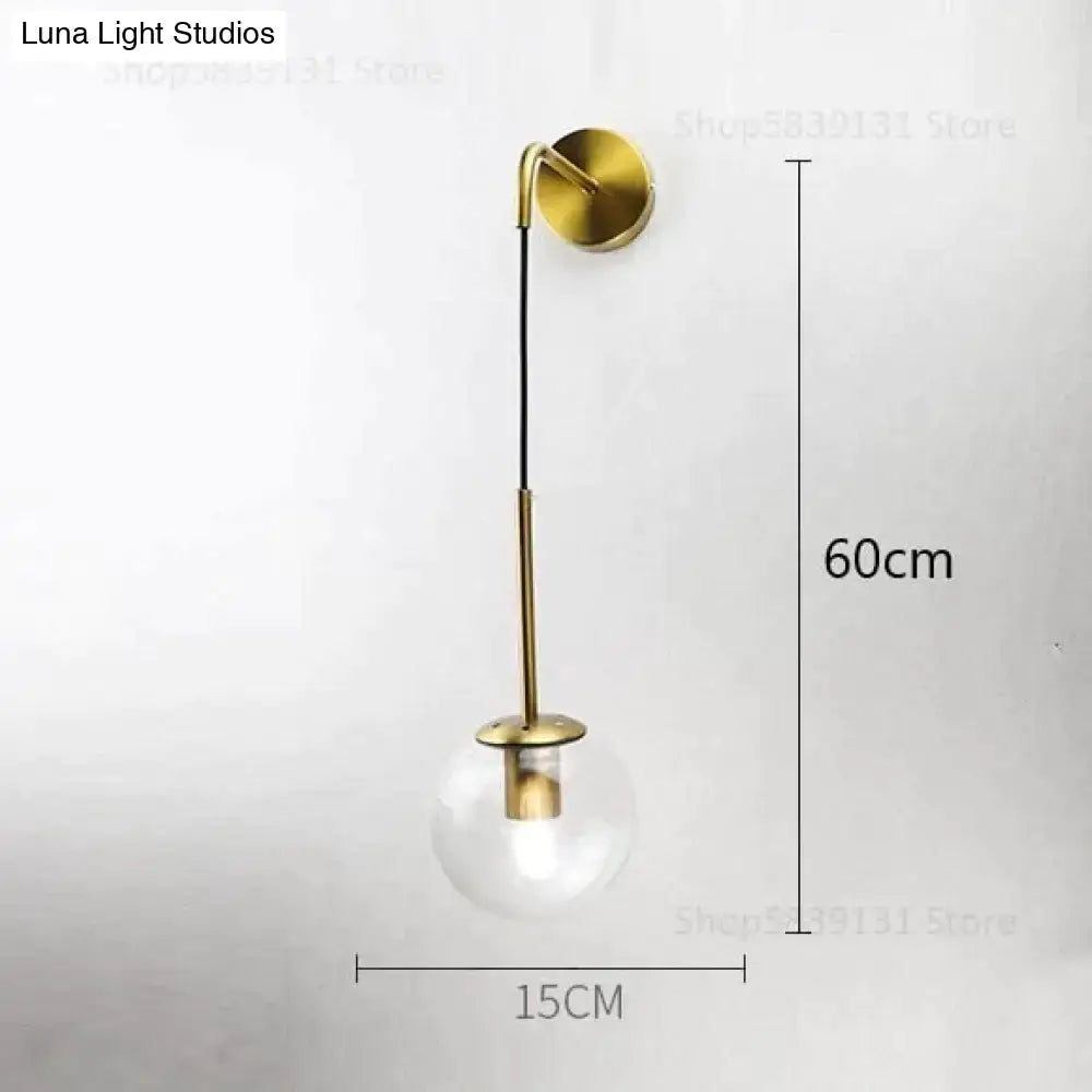 A sleek brass-finished nordic retro modern wall lamp with minimalist curved arm and clear glass smoked globe bulb