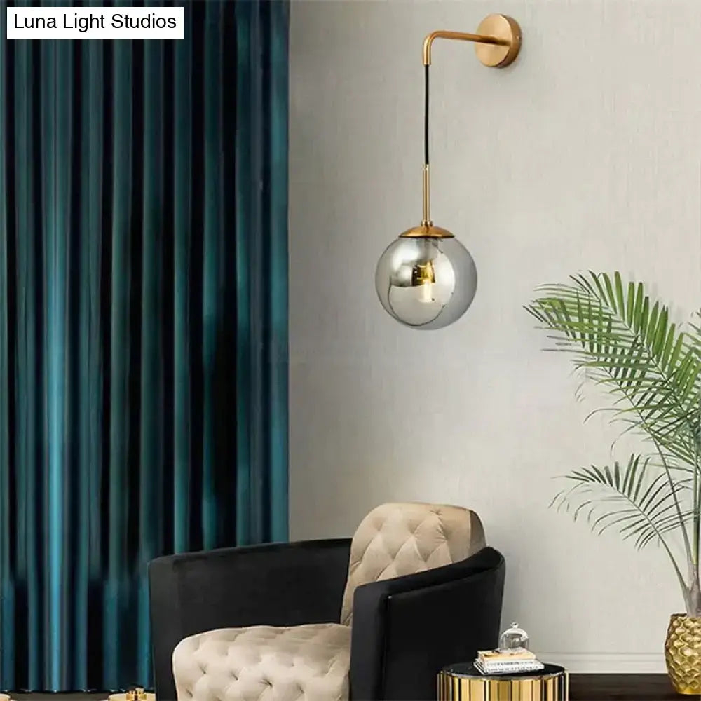 A sleek retro modern glass smoked globe wall lamp with gold-toned metal arm for bedroom lighting