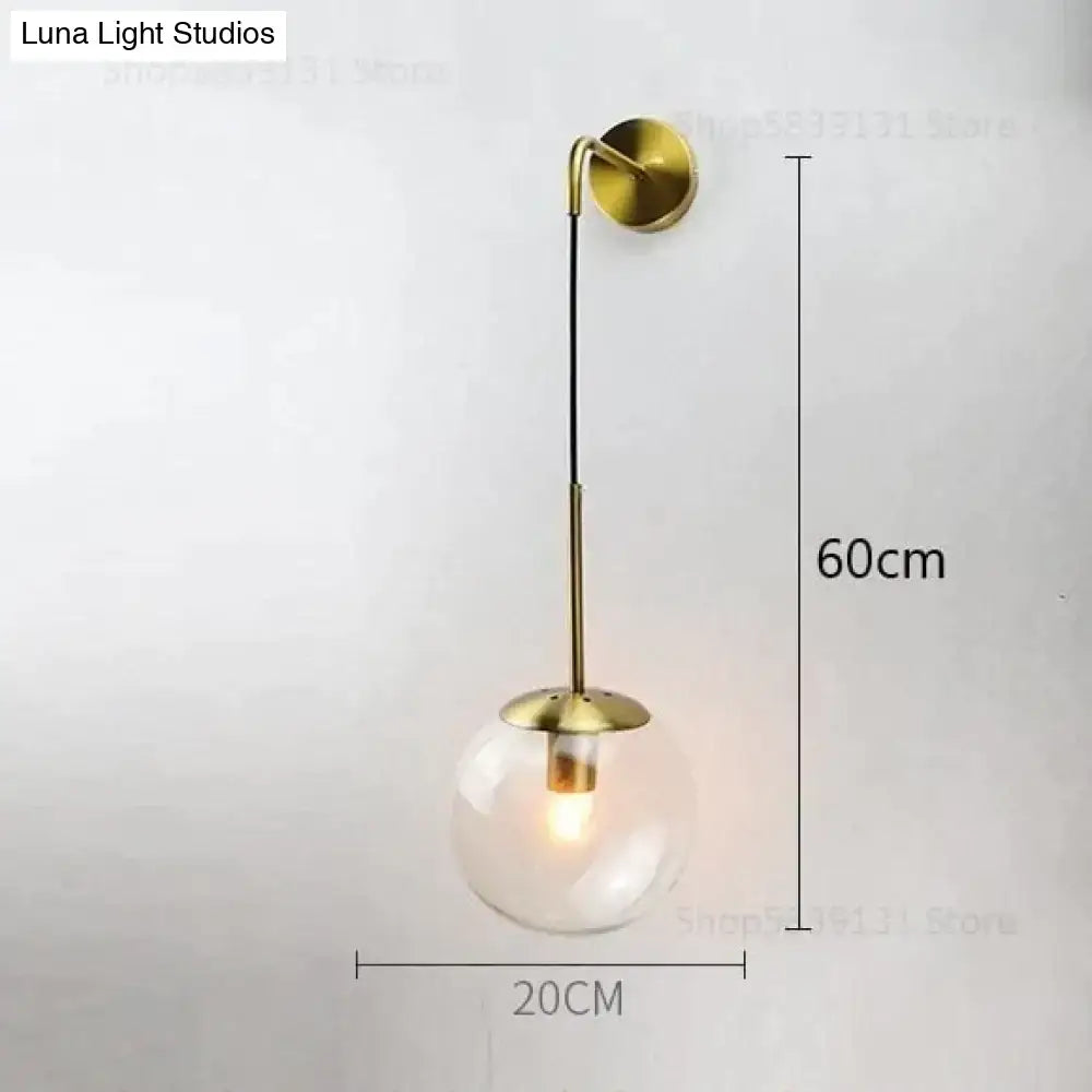 A sleek brass-finished retro modern glass wall lamp with clear globe and slender stem for bedroom lighting