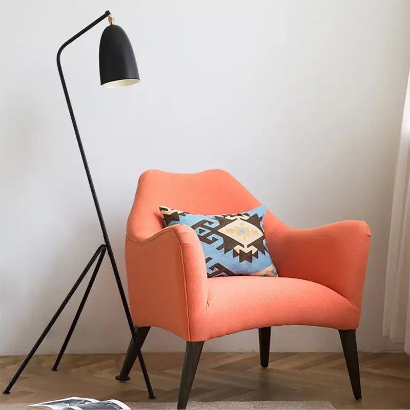 Orange upholstered armchair with geometric pillow next to retro nordic decorbites grasshopper floor lamp for living room decor