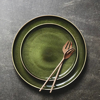 Set of two retro olive green ceramic dinner plates with matte finish and gold rim accompanied by wooden utensils