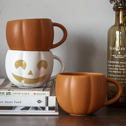 Two retro orange pumpkin ceramic mugs with white base, gold jack o lantern face, and enamel handle for halloween use