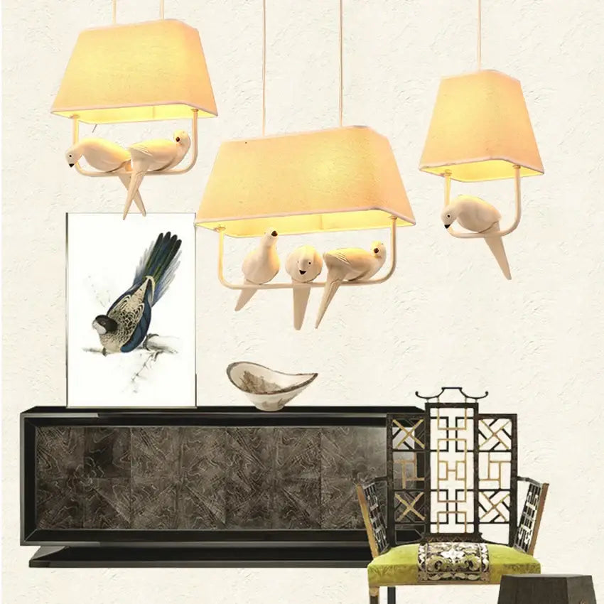 Three warm-toned fabric shade pendant lights with white ceramic birds on metal frames in a retro white resin bird cage chandelier
