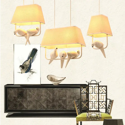 Three warm-toned fabric shade pendant lights with white ceramic birds on metal frames in a retro white resin bird cage chandelier