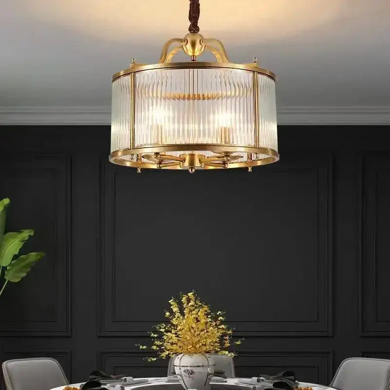 A gold-toned decorbites glass chandelier with vertical ribbed panels suspended by a twisted brown cord