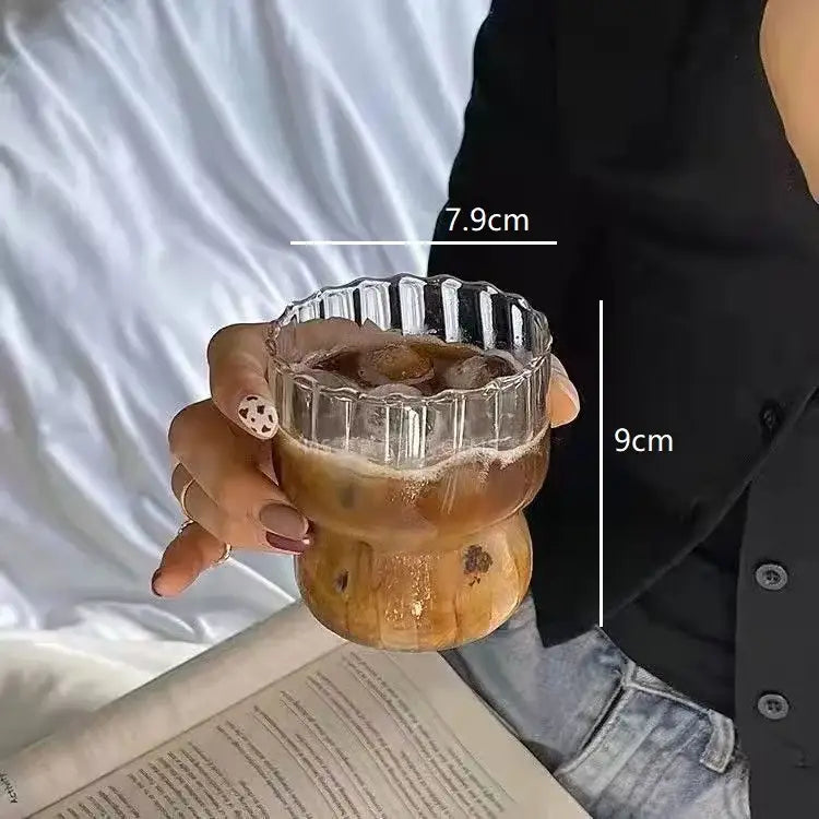 A clear ribbed glass cup with wooden base holding iced coffee from decorbites clear glass coffee tumbler set