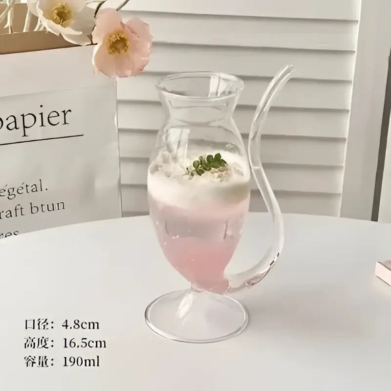 A clear glass mug with a curved handle filled with pink liquid topped with foam and green garnish decorbites heart love
