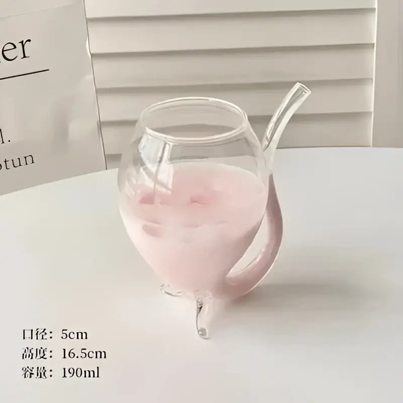 A clear glass pitcher with a curved handle and three feet filled with pink liquid complements decorbites heart love glass mugs