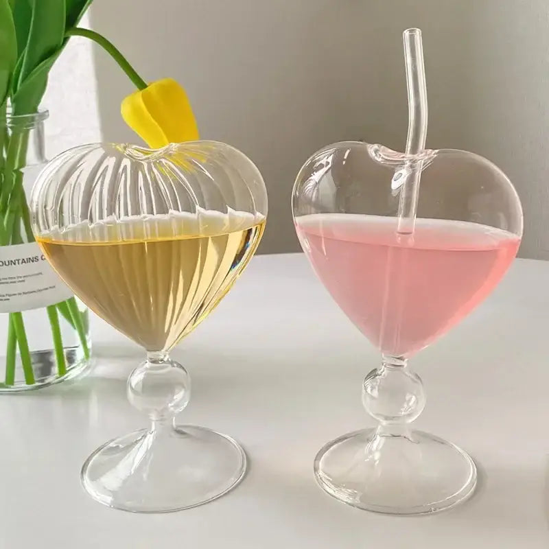 Two clear ribbed heart love glass mugs by decorbites with spherical base filled with golden and pink liquid
