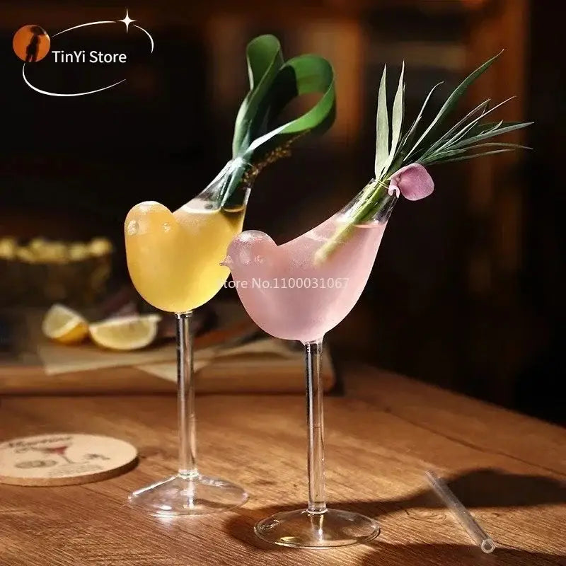 Two elegant clear glass mugs shaped like birds with yellow and pink drinks and green garnish by decorbites heart love