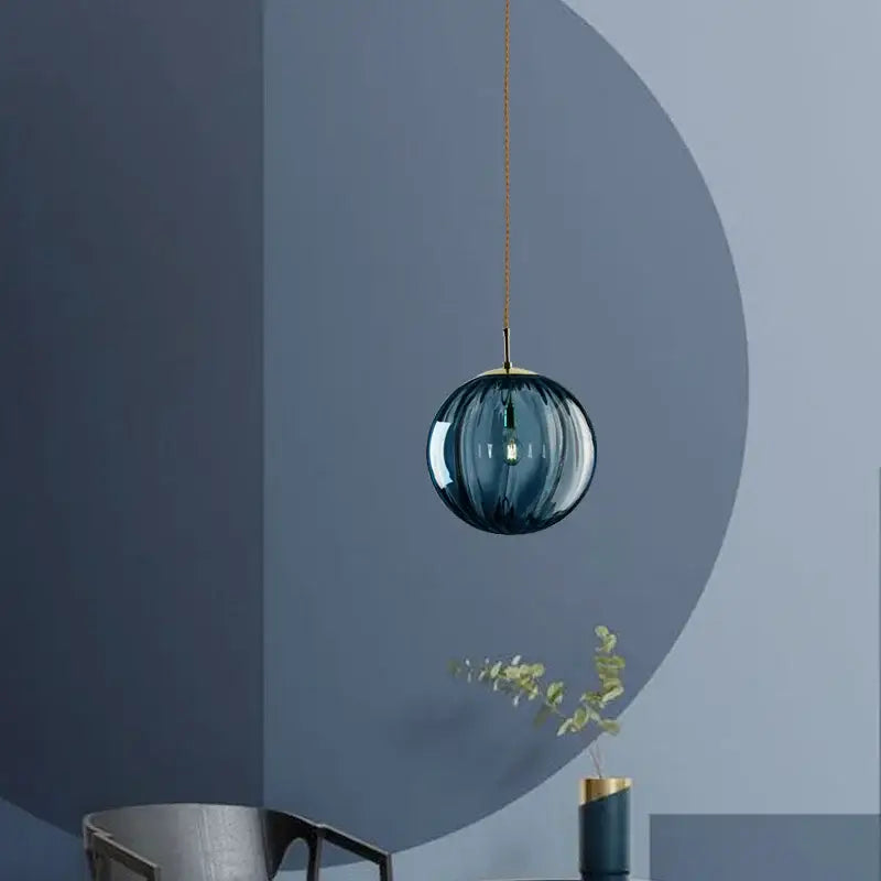 A sleek spherical blue glass globe pendant light with gold chain and iron finish for dining room use
