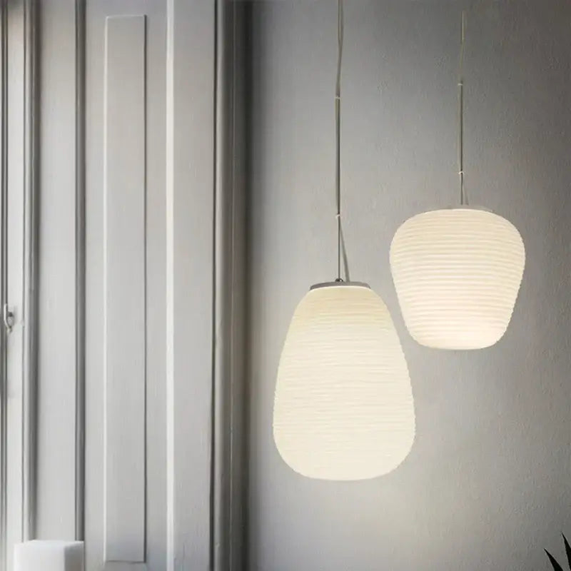 Two off-white ribbed glass cocoon pendant lights with slender metal chains hang against a gray wall for dining room decorbites pendant light