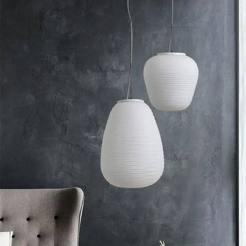 Two off-white ribbed paper pendant lights hang against a dark wall decorbites glass cocoon pendant light kitchen lamp