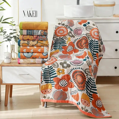 A vibrant orange and teal floral-patterned cotton bath towel with a white base draped over a chair back
