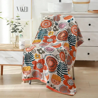 A cozy cream-colored cotton bath towel with vibrant orange teal and yellow floral pattern draped over a chair