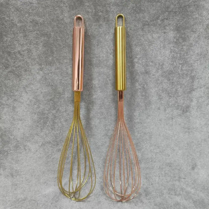 Two metallic wire egg beaters with rose gold and brass-colored decorbites gold steel handles for kitchen use