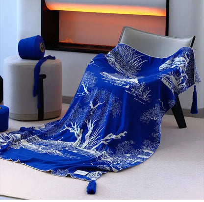 A vibrant royal blue and white knitted sofa blanket with intricate landscape patterns and tassels for living room use