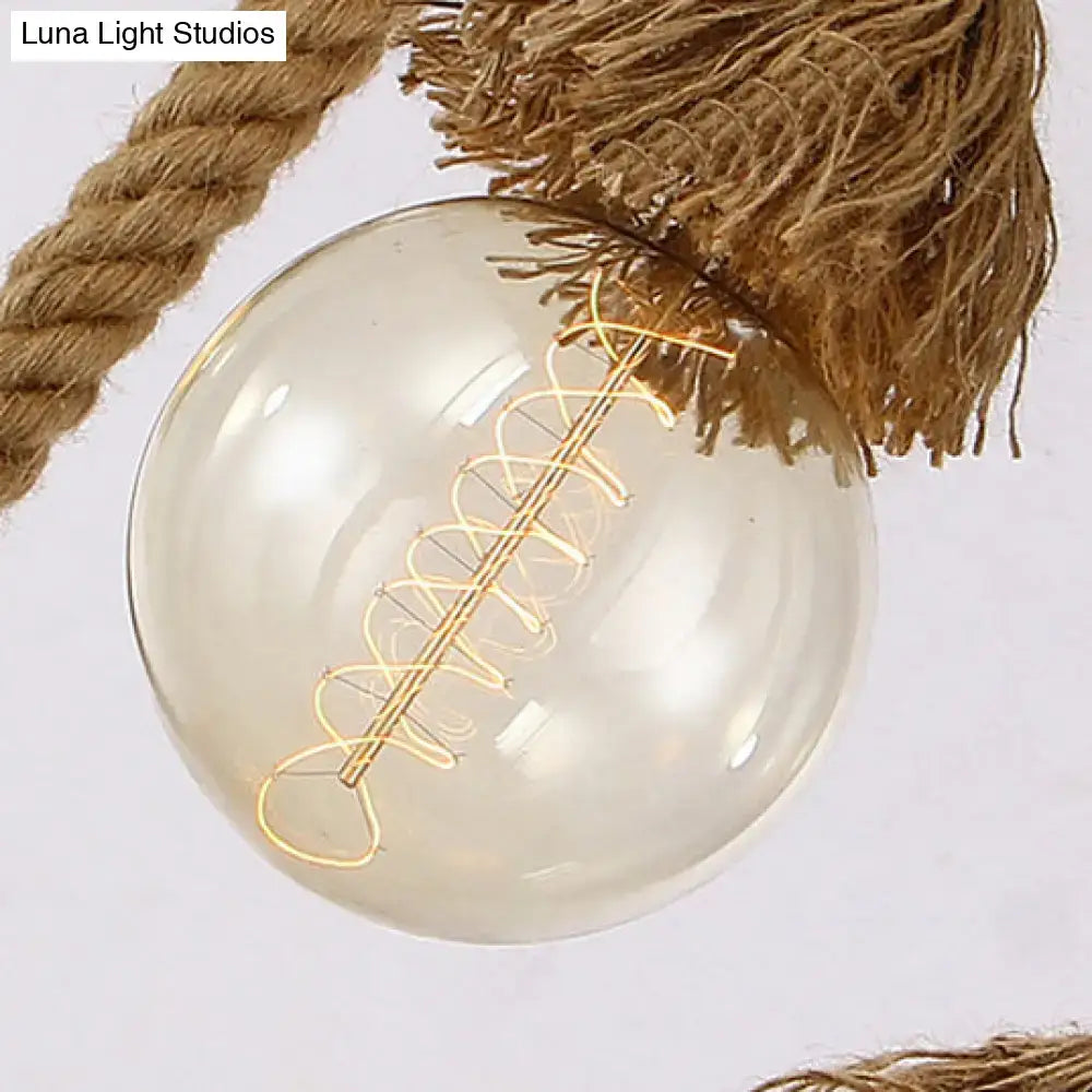 Clear glass globe with coiled filament suspended by beige adjustable rope island light with tassels and bamboo details