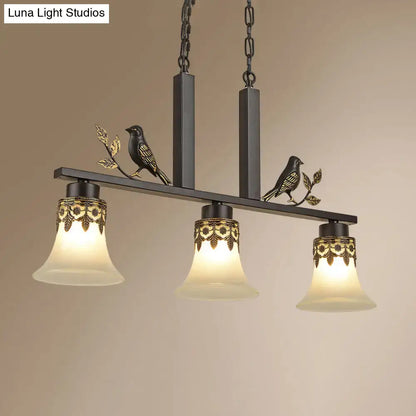 Black metal island light fixture with ornate gold leaf detailing and three frosted glass shades for dining room