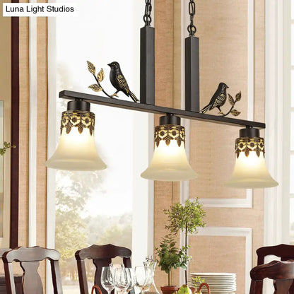 Black metal island light fixture with ornate gold detailing and three frosted glass shades featuring decorative birds