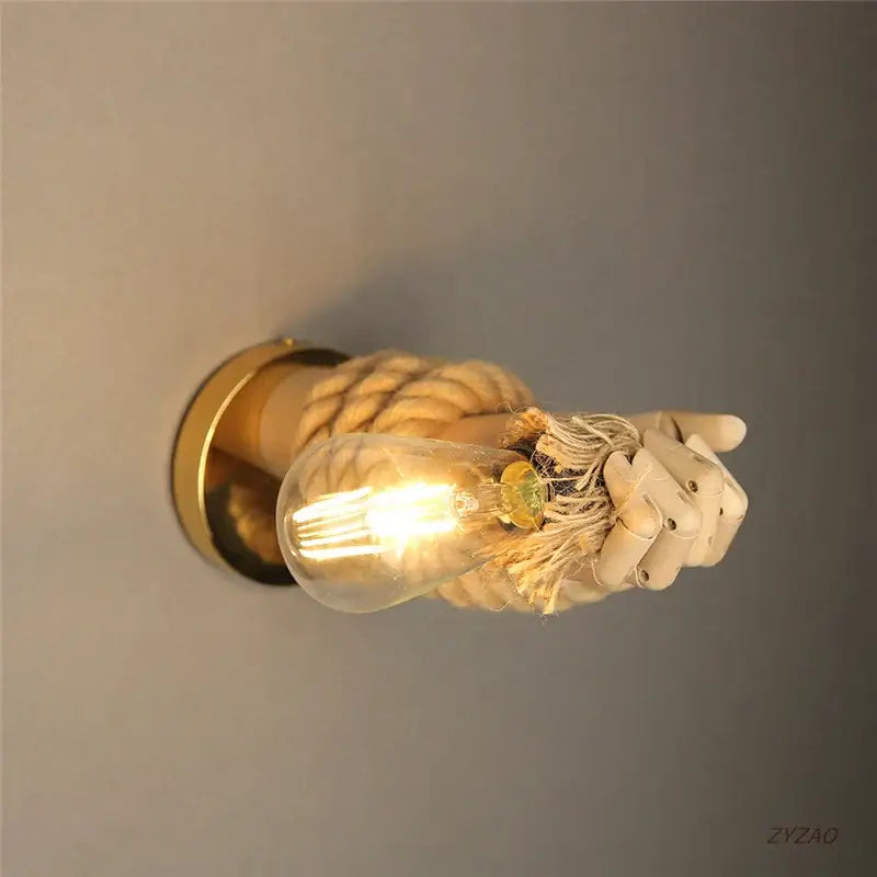 Rustic brass hand shape wall lamp with beige articulated hand gripping hemp rope and exposed filament bulb wall light