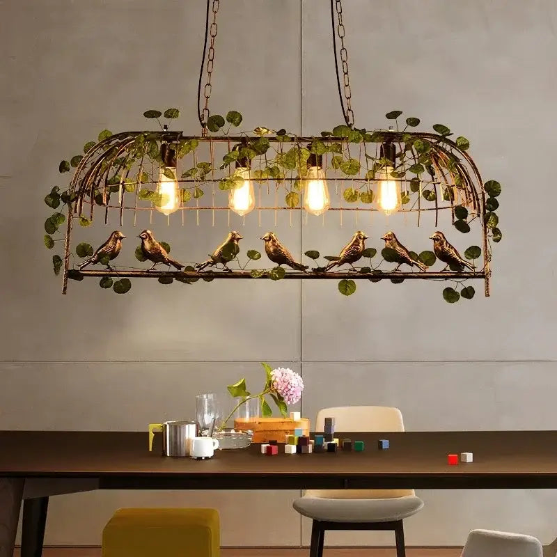 Rustic bronze bird cage chandelier featuring exposed filament bulbs and hanging greenery with green leaf bird accents