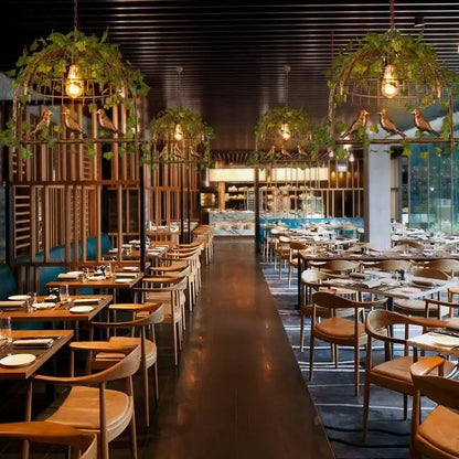 Rustic bronze green leaf bird cage chandelier above wooden tables and chairs with brown leather seats in modern dining room