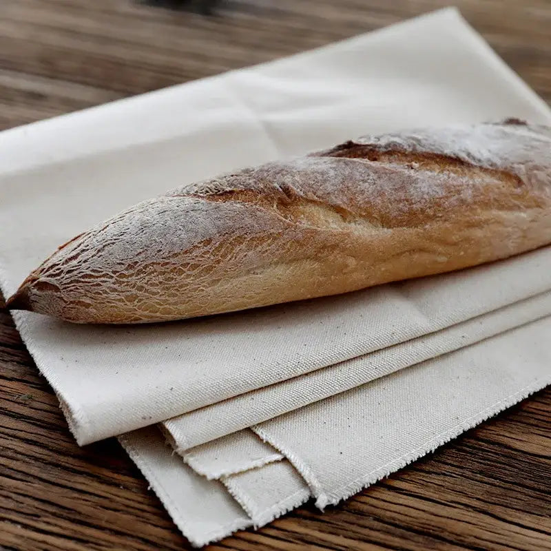 Golden-brown baguette on rustic off-white decorbites linen flax cloth baking mat with a dusting of flour and cracked crust