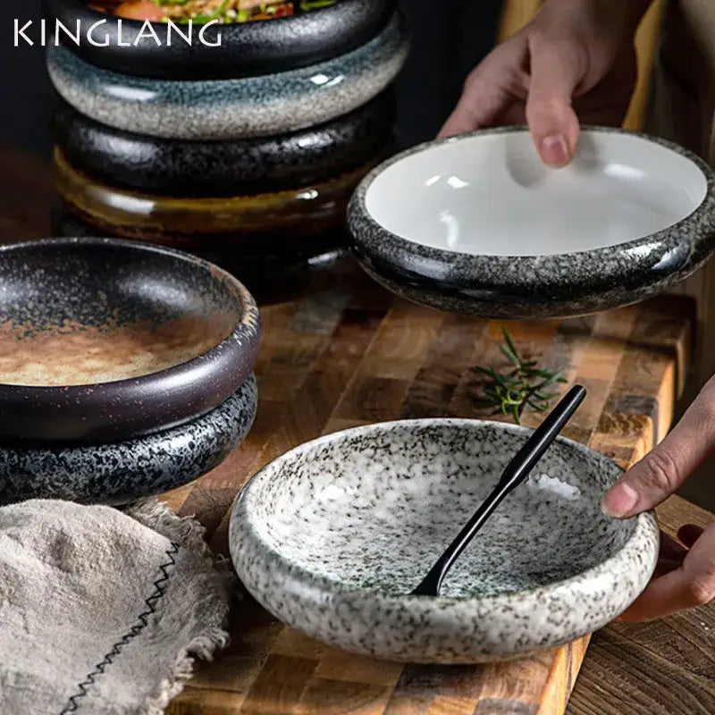 A rustic speckled ceramic kimchi plate with a glossy black rim and white interior for dining use