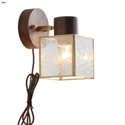 Rustic walnut wood wall sconce with dark wood backplate brass accents and frosted glass panels for bedroom use