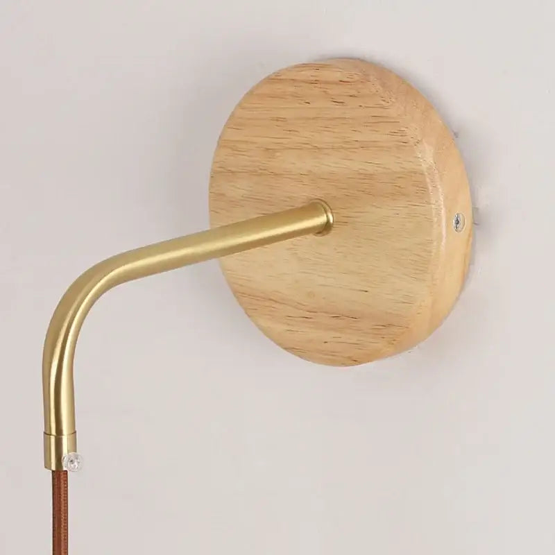 Minimalist wall light with round light wood backplate, curved brass arm, and clear glass pull chain switch