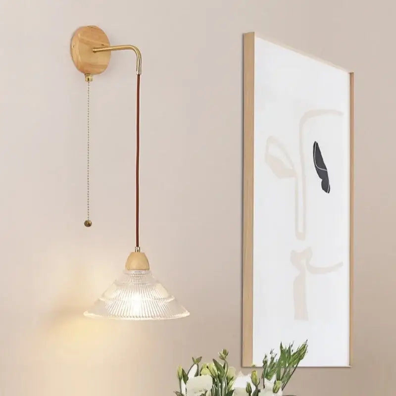 Rustic wood and brass wall light with clear glass shade and pull chain switch featuring a curved brass arm and wooden base