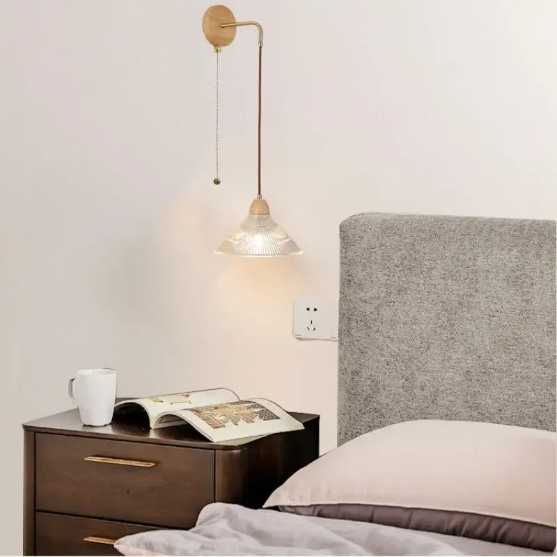 Minimalist brass wall light with wooden base and clear glass pull chain switch featuring a textured glass shade